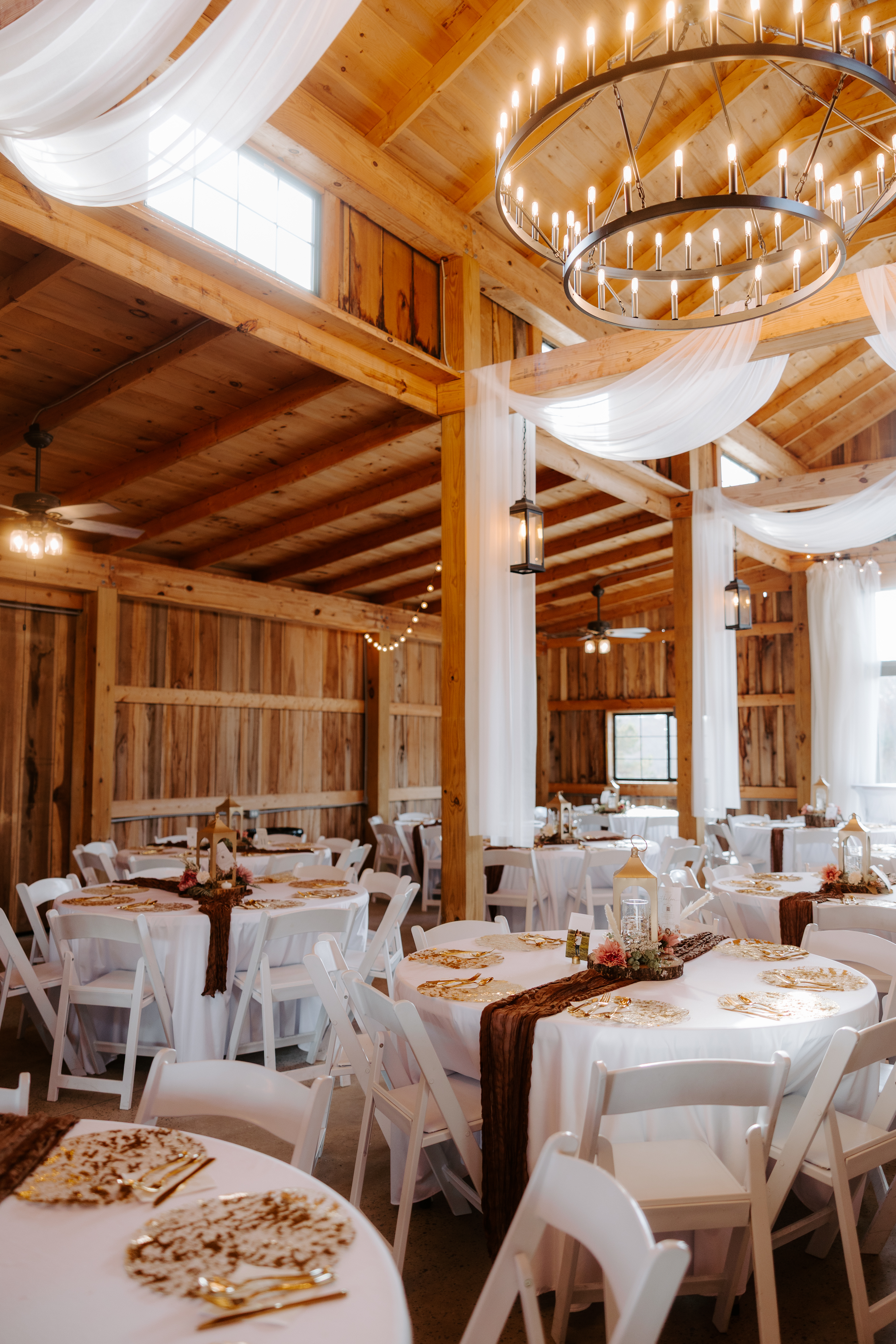 Cedar Hills Farm reception barn interior set for a fall wedding with round tables, white linens, dark brown table runners, and ring chandeliers overhead between exposed wood beams