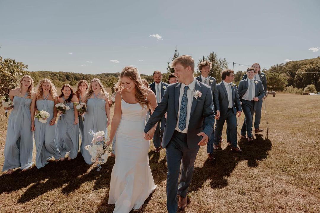 Bride and groom leading their full wedding party across the ceremony lawn at Cedar Hills Farm on a sunny summer day