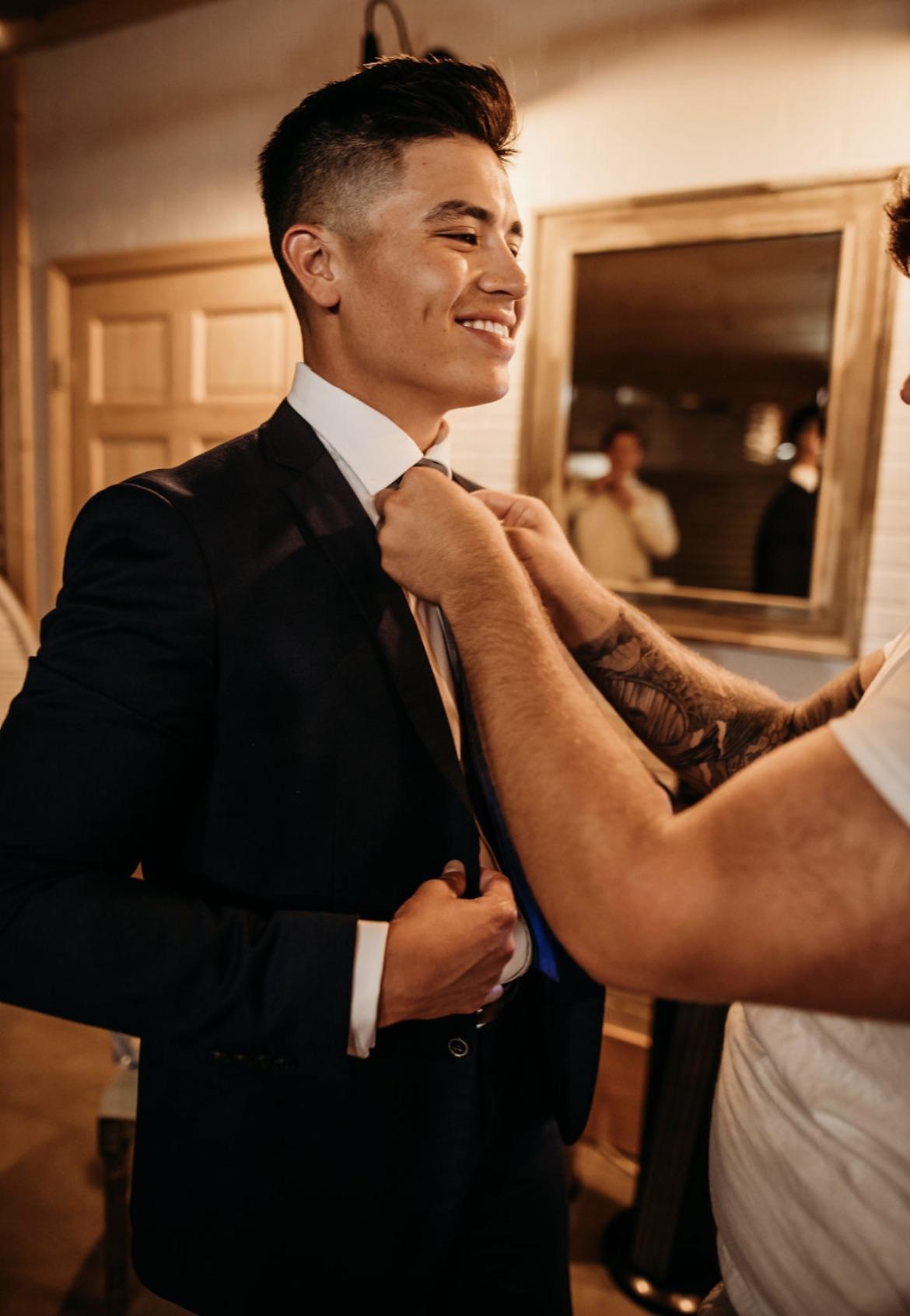 Groom getting his tie adjusted by a groomsman in the groom's suite at Cedar Hills Farm