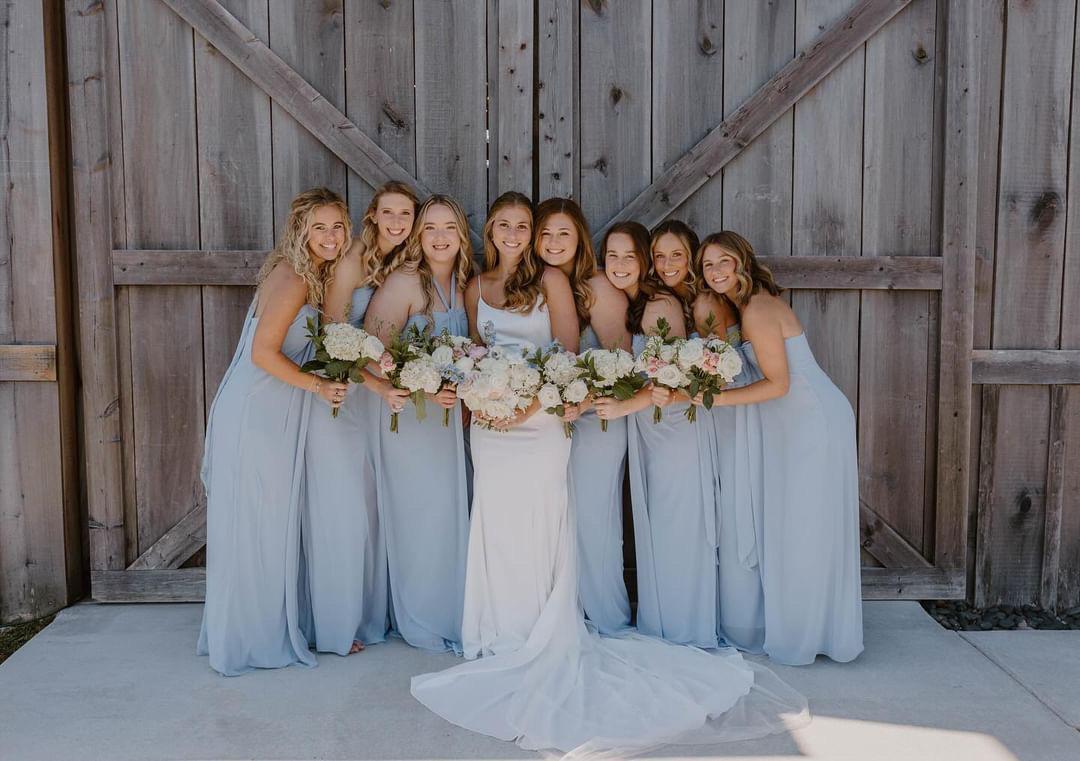 Bride and bridesmaids in light blue dresses posing in front of the barn doors at Cedar Hills Farm