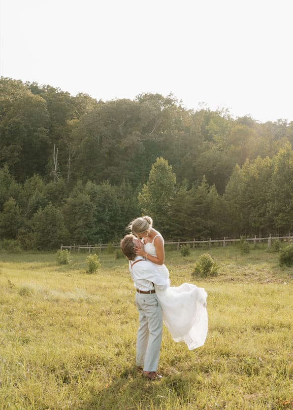 Groom lifting his bride into the air in the open sunny meadow at Cedar Hills Farm during couple portraits