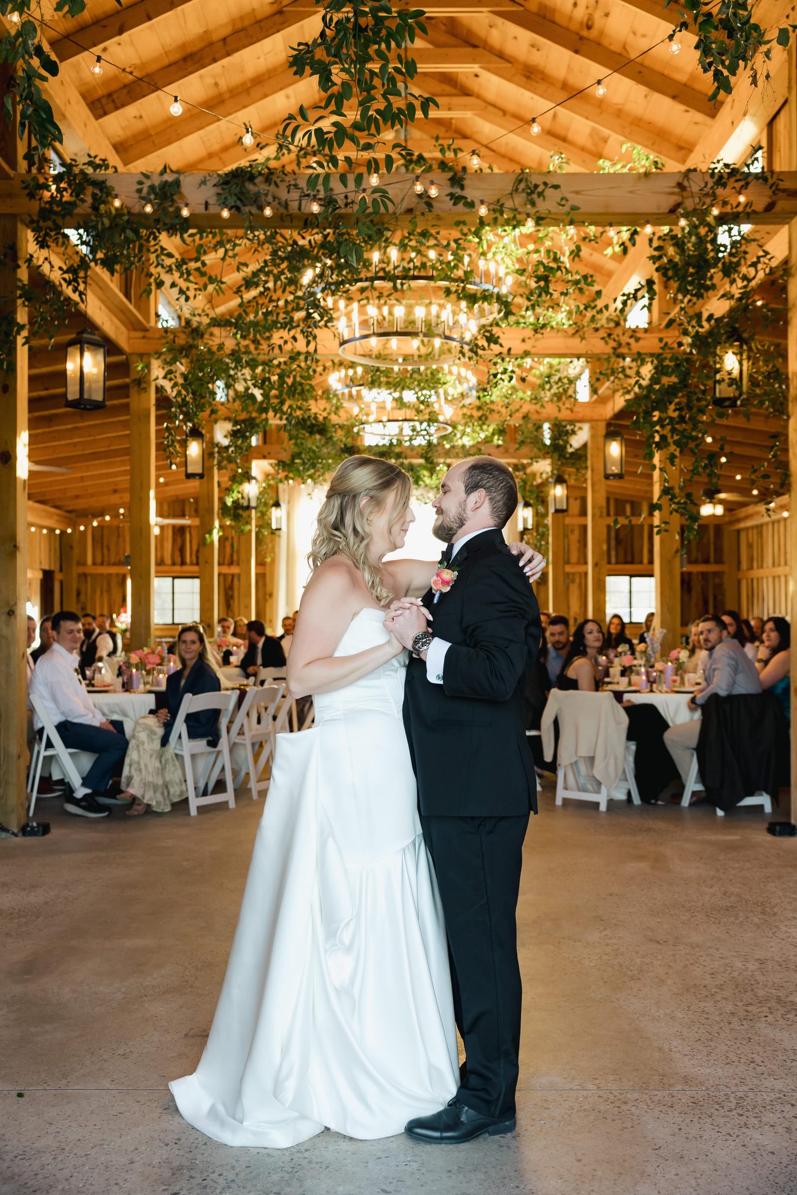 Bride and groom first dance inside the reception barn at Cedar Hills Farm with hanging greenery and ring chandeliers