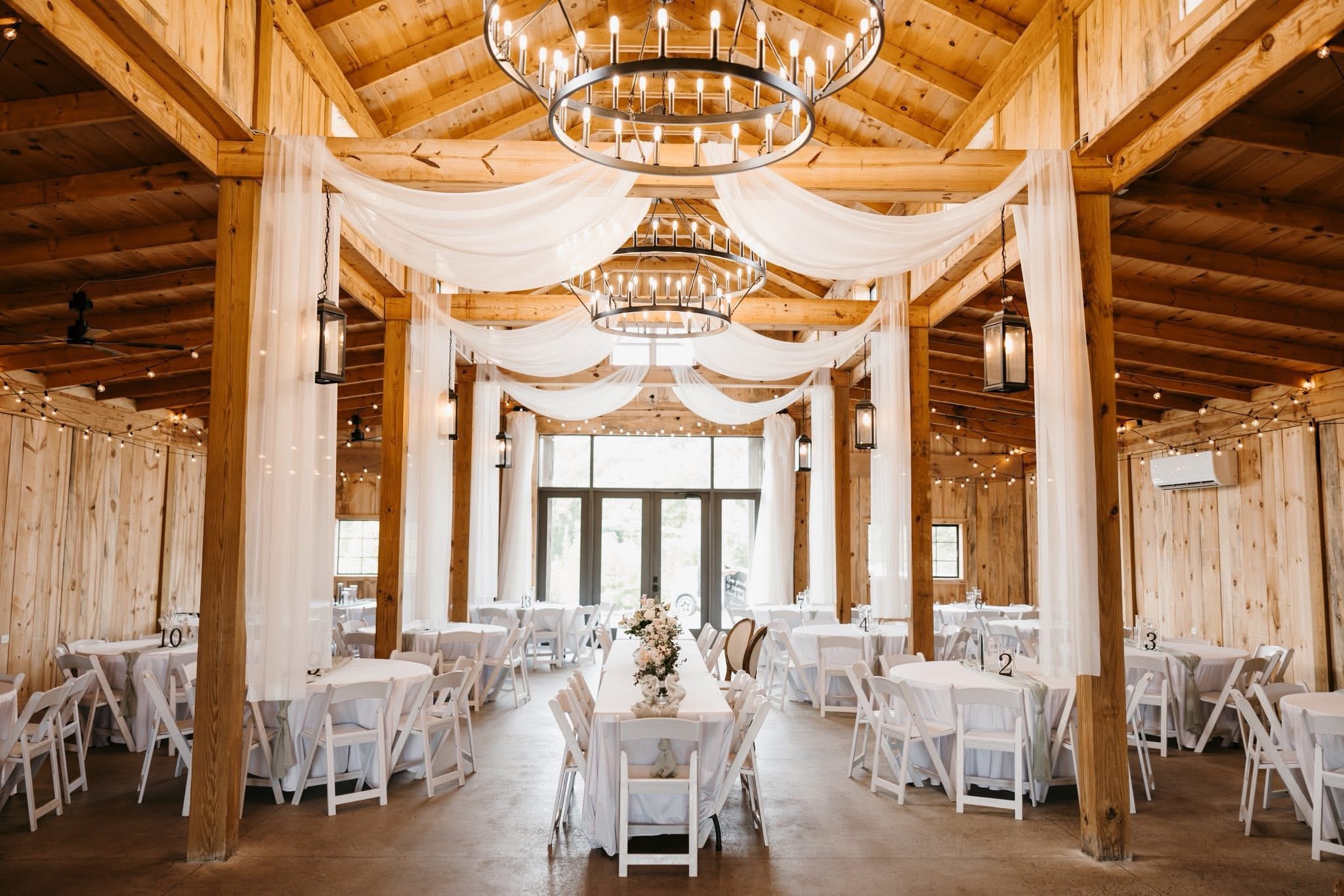 Cedar Hills Farm reception barn interior dressed with white fabric draping and ring chandeliers