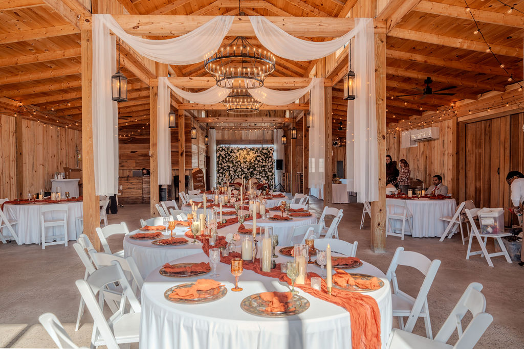 Cedar Hills Farm reception barn interior set for a fall wedding with terracotta table linens, candlelight, and ring chandeliers overhead