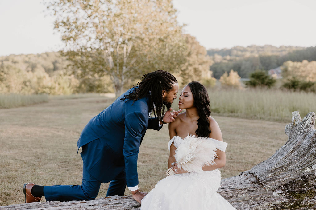 Groom kneeling at the driftwood log to kiss his bride at golden hour at Cedar Hills Farm