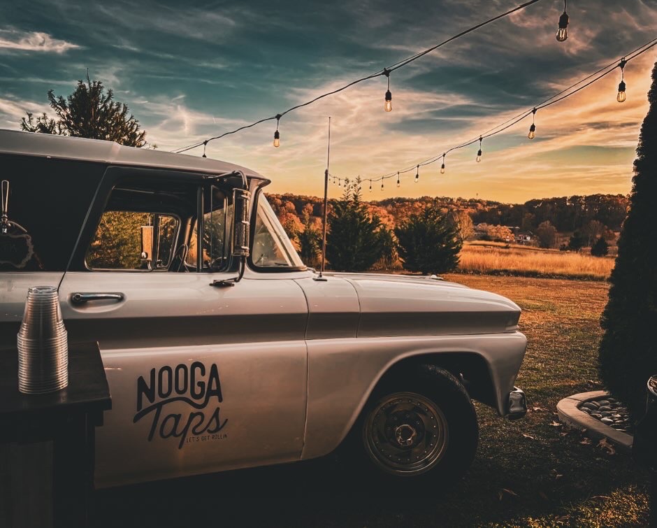 Nooga Taps mobile bar truck parked on the Cedar Hills Farm lawn at sunset with string lights overhead